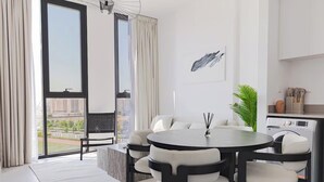 En moderne stue med et rundt spisebord, en sofa og et stort vindue med udsigt over byen.