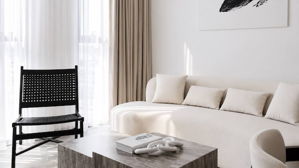 Et moderne hotelværelse med en seng, en sort stol med perforeringer, et sofabord med en bog og en væg med et indrammet kunstværk.