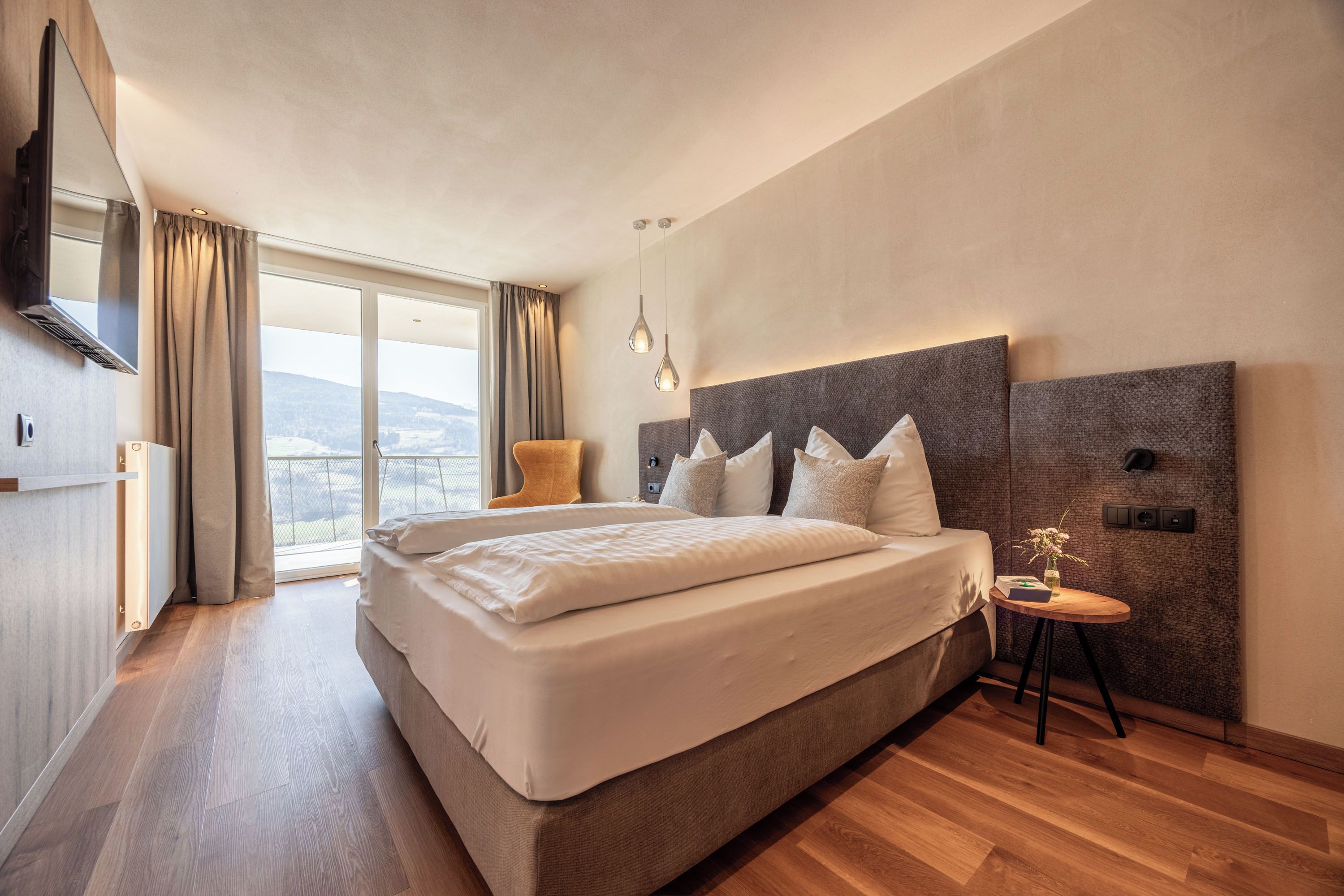 Habitació d'hotel moderna amb un llit gran, vistes a l'exterior i una taula petita amb un vas.