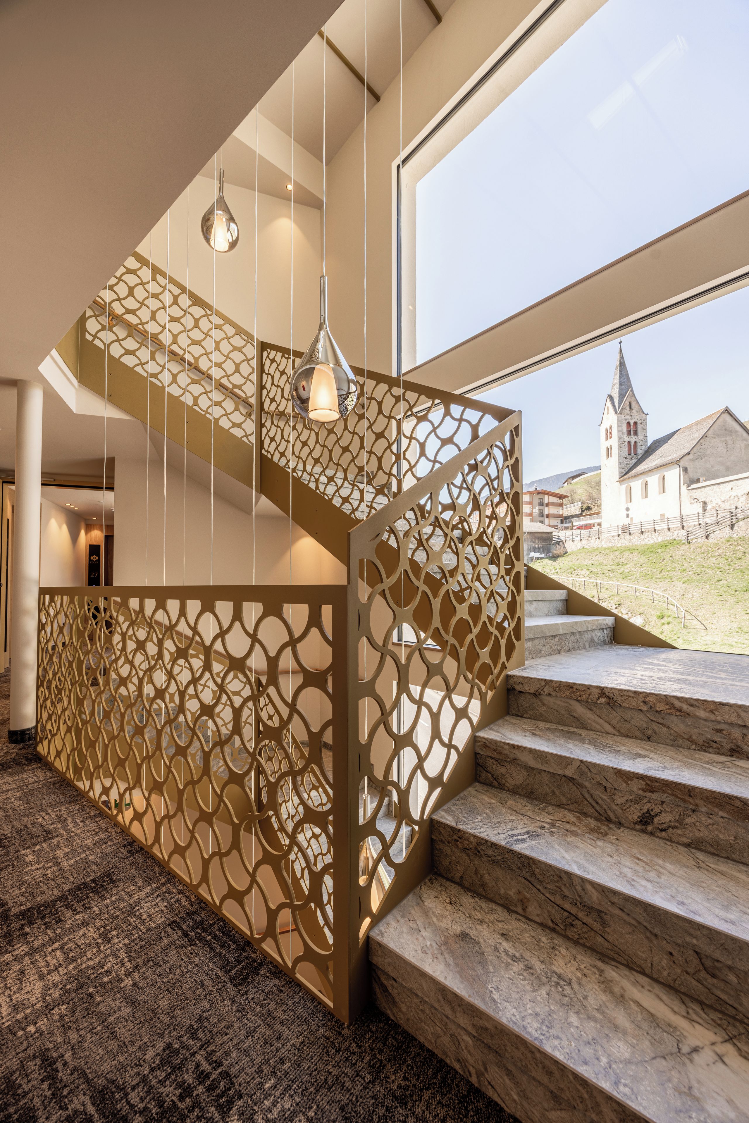 A modern interior with a staircase featuring a geometric patterned railing and a view of a church outside.