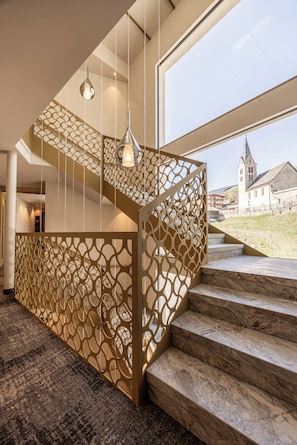 A modern interior with a staircase featuring a geometric patterned railing and a view of a church outside.