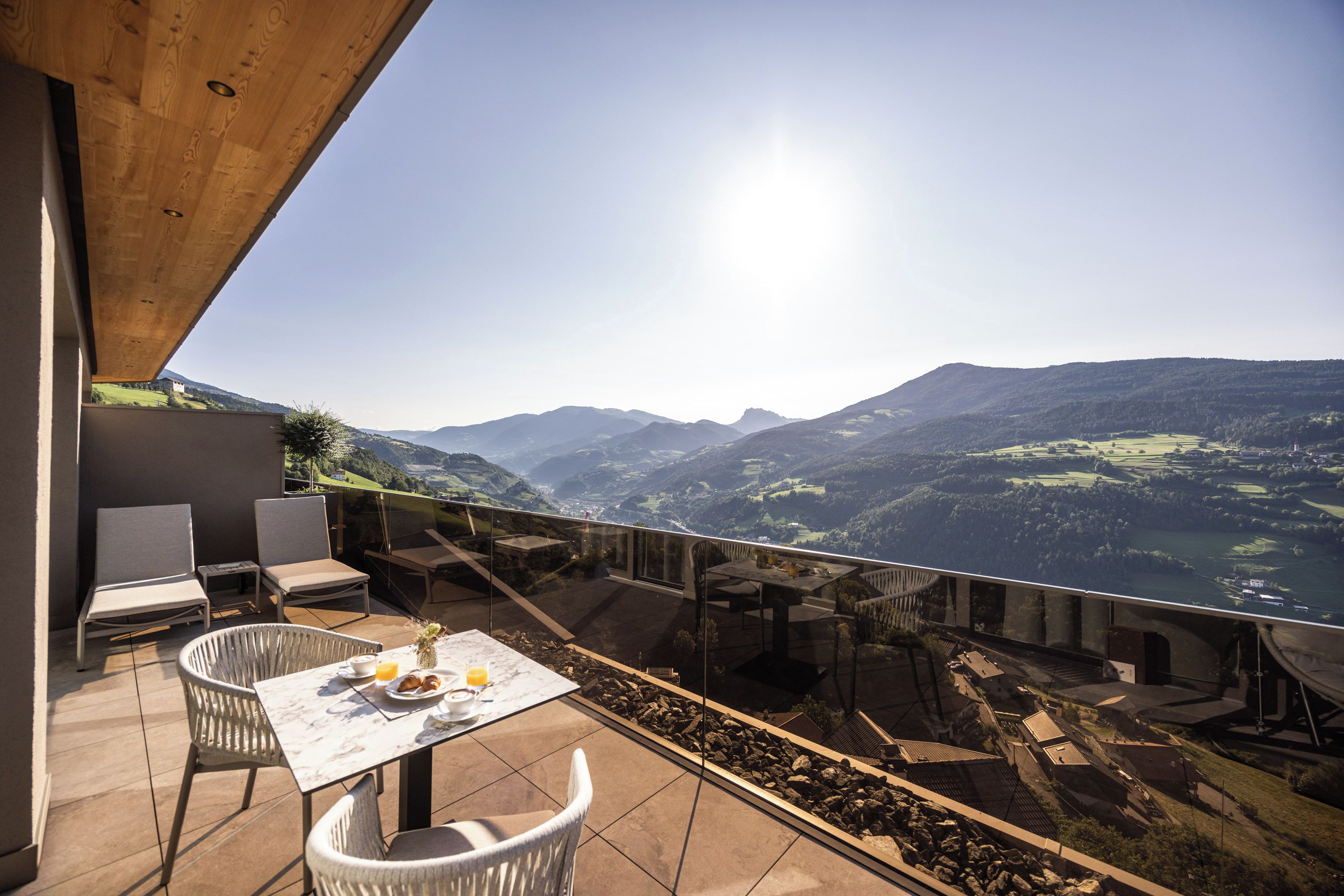 A terrace with a table set for two, overlooking a valley with mountains.