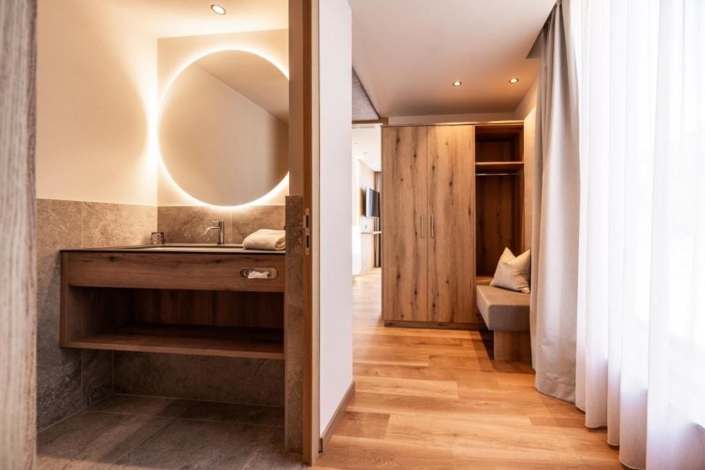 A modern bathroom with a wooden vanity, a round mirror, and a built-in bench.