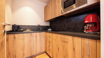 A modern kitchen with wooden cabinets, a black countertop, a stainless steel microwave, and a red coffee maker.