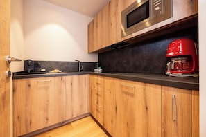 A modern kitchen with wooden cabinets, a black countertop, a stainless steel microwave, and a red coffee maker.