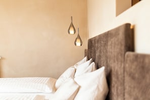 A bed with white bedding and a headboard, two pendant lights, and a plain wall.