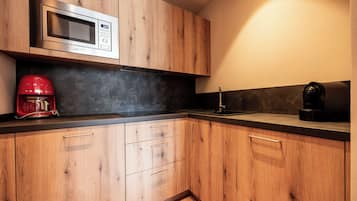 A kitchen with wooden cabinets, a stainless steel microwave, a red coffee maker, and a black coffee machine.