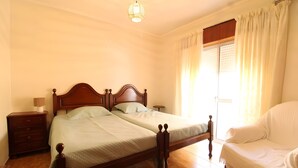 Ein Schlafzimmer mit einem Doppelbett, einem Nachttisch, einer Lampe, einem Sessel und einem Fenster mit Vorhängen.