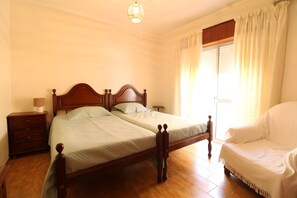 Un dormitorio con una cama doble, una mesita de noche, una lámpara, una silla y un ventanal con cortinas.