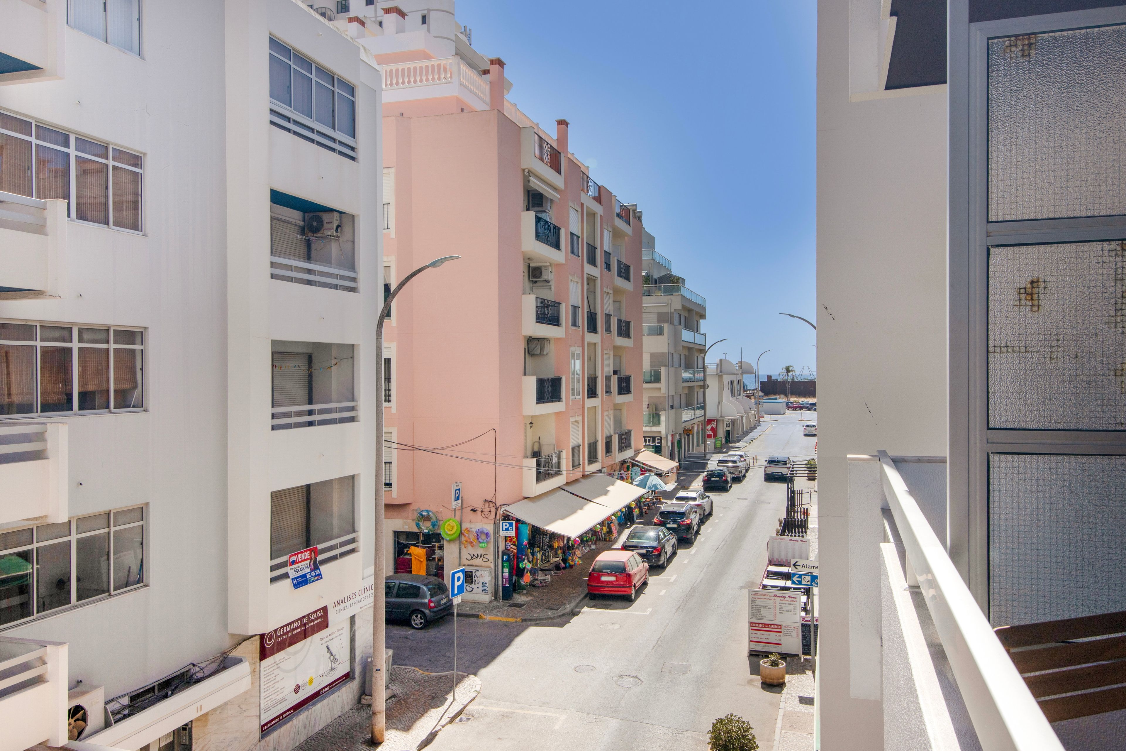 Vista de la calle con edificios de varios pisos, cielo despejado y automóviles estacionados.