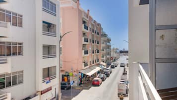 Vista de la calle con edificios de varios pisos, cielo despejado y automóviles estacionados.