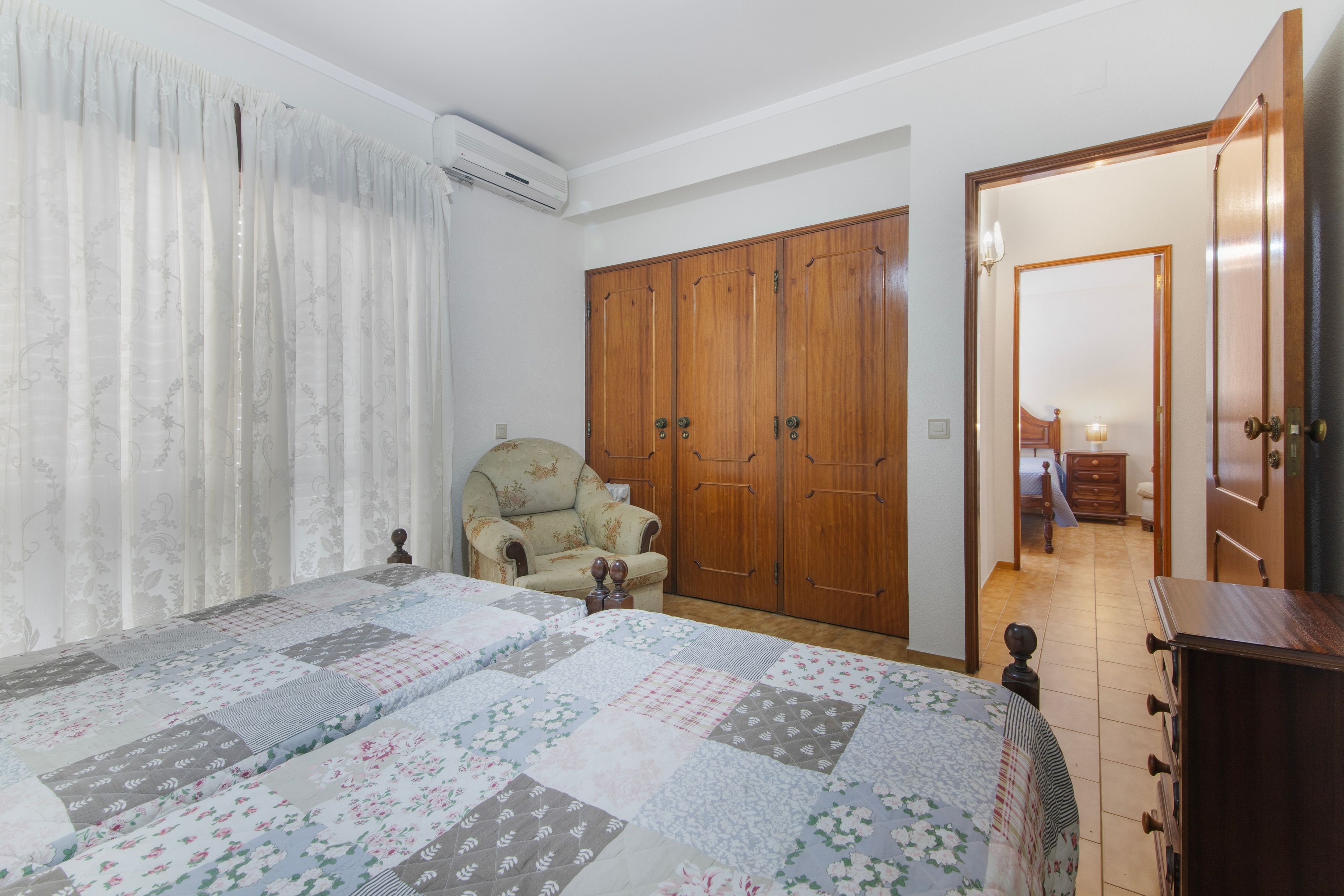Een slaapkamer met een groot bed, een houten garderobe, een stoel en een airconditioning.