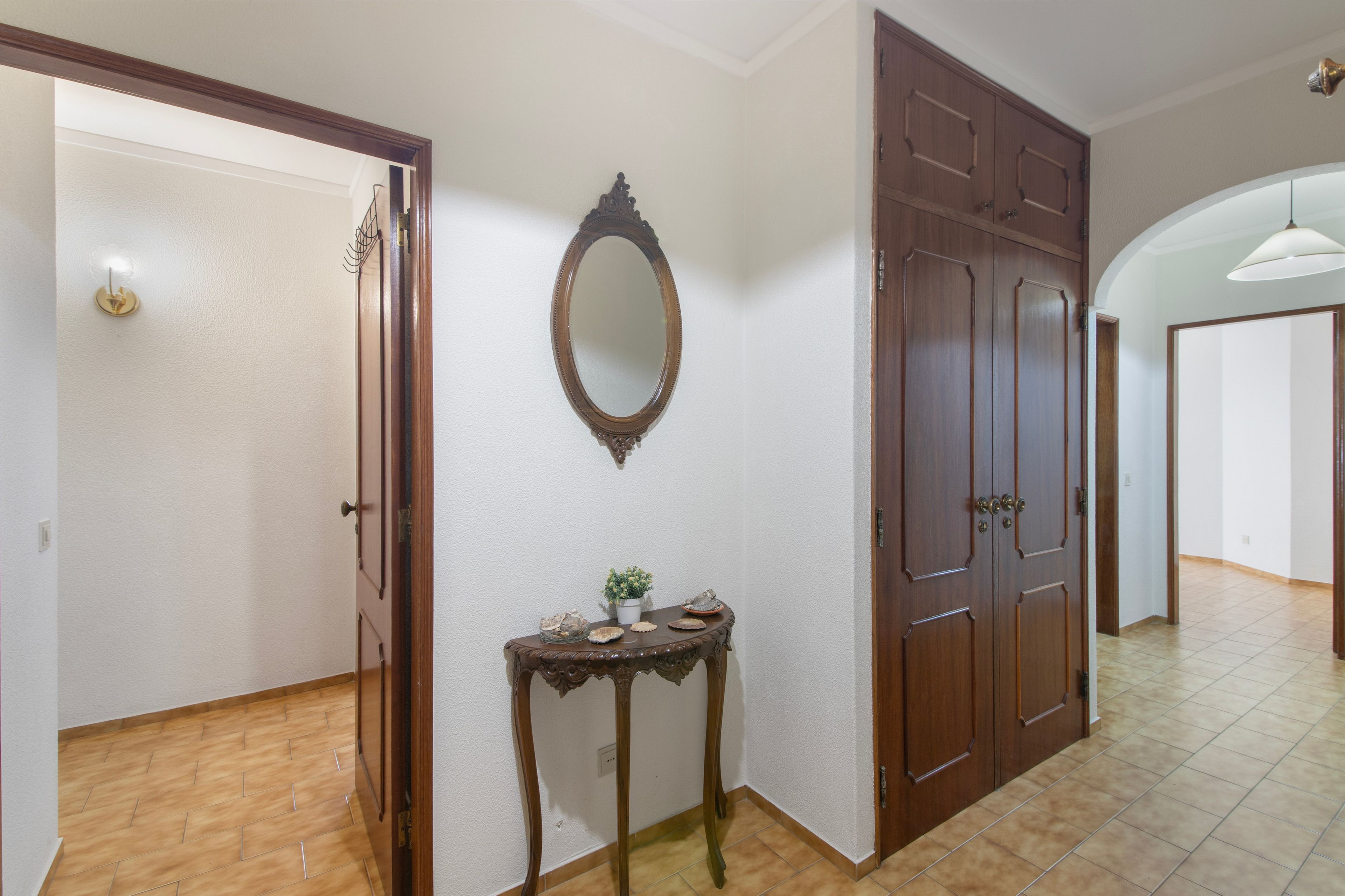 Un couloir avec une porte en bois, un miroir et une petite table ornée d’objets décoratifs.