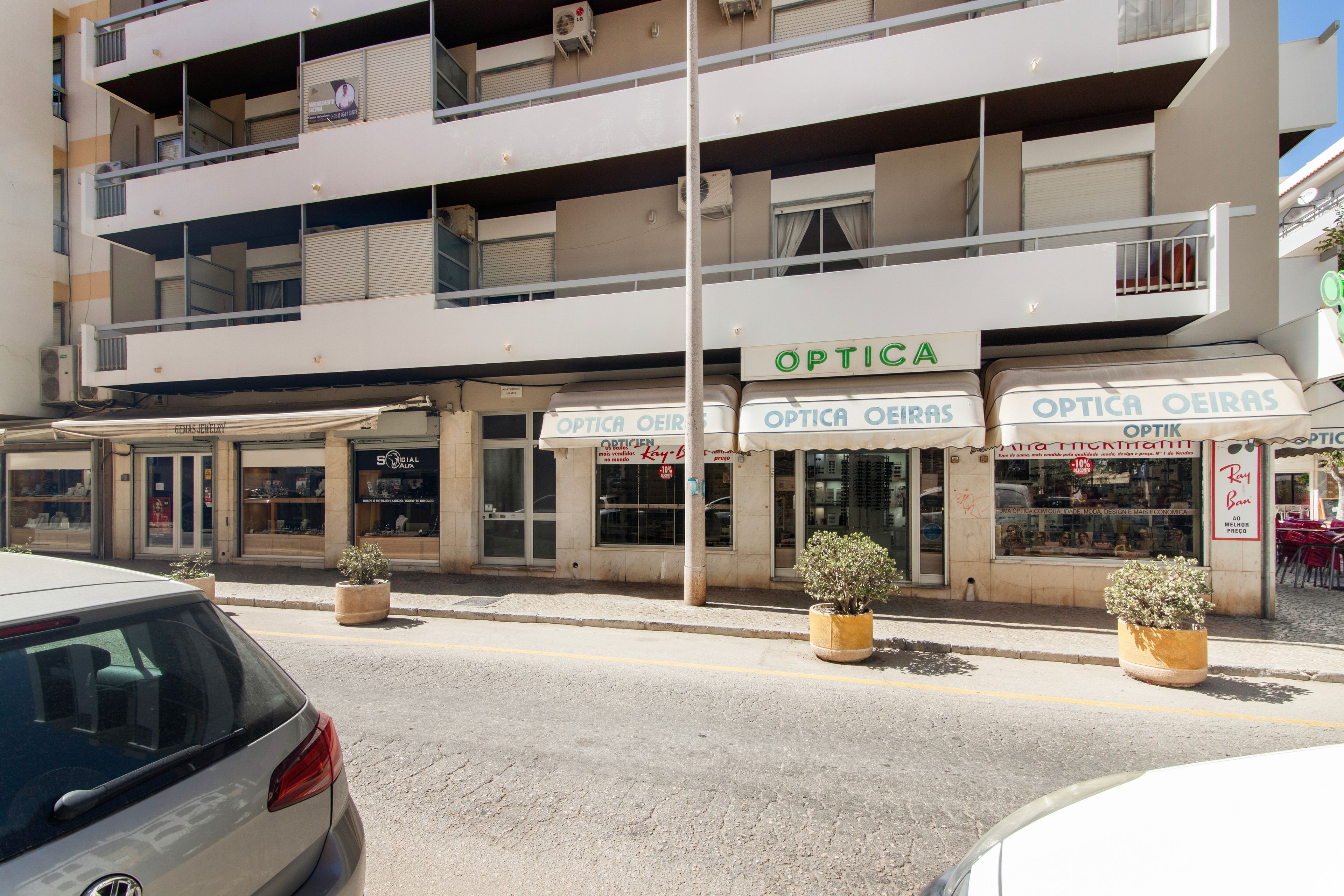 Un edificio de varios pisos con locales comerciales, incluyendo una óptica llamada 'OPTICA OEIRAS' y una tienda de redes sociales llamada 'SOCIAL ALFA'.