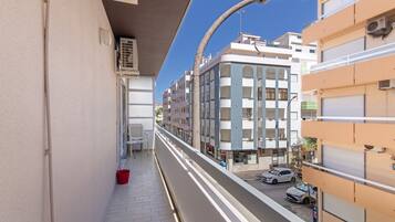 A narrow urban street with buildings on either side, a clear sky, and parked cars.