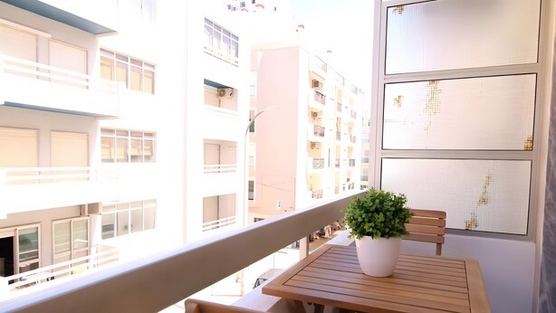 Ein Balkon mit einem Holztisch und Stühlen, einem Blumentopf und Blick auf angrenzende Gebäude.