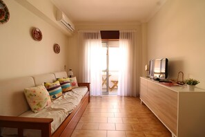 Una sala de estar con sofá, televisor sobre un mueble bajo, una mesita y una ventana con cortinas.