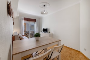 A compact dining area with a wooden table, chairs, a potted plant, and a television on a stand. - Apartment 'Ocean Stay Ap' with Balcony, Wi-Fi and Air Conditioning (Monte Gordo)
