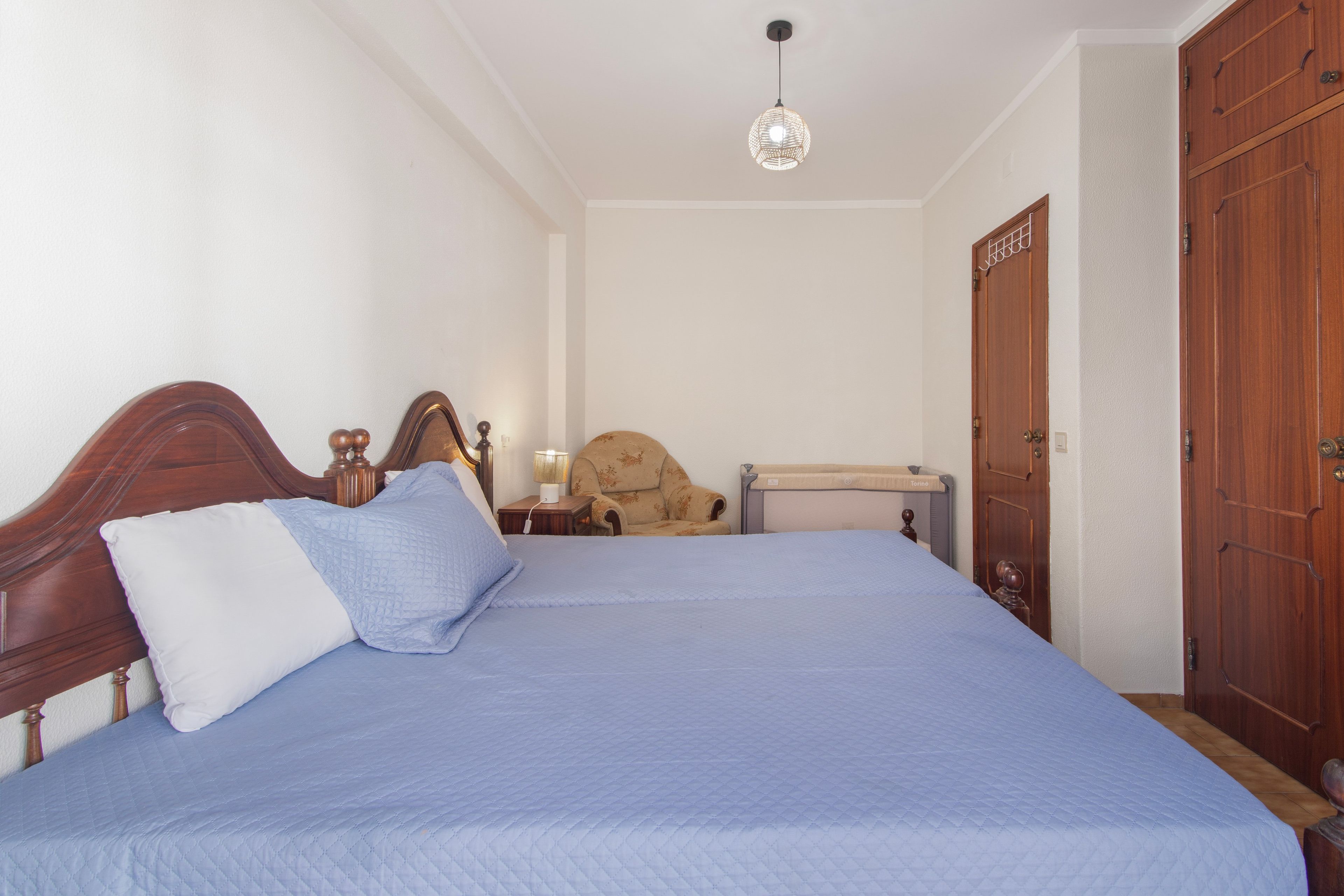 Un dormitorio con cama, mesita de noche, silla, armario e iluminación colgante.