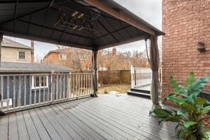 A covered outdoor deck with a metal railing, a brick wall, and a view of a residential area. - Executive 5BR Rose Bloom Haven with Private Deck (Mississauga)