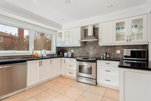 A modern kitchen with white cabinetry, stainless steel appliances, and a tiled backsplash. - Executive 5BR Rose Bloom Haven with Private Deck (Mississauga)