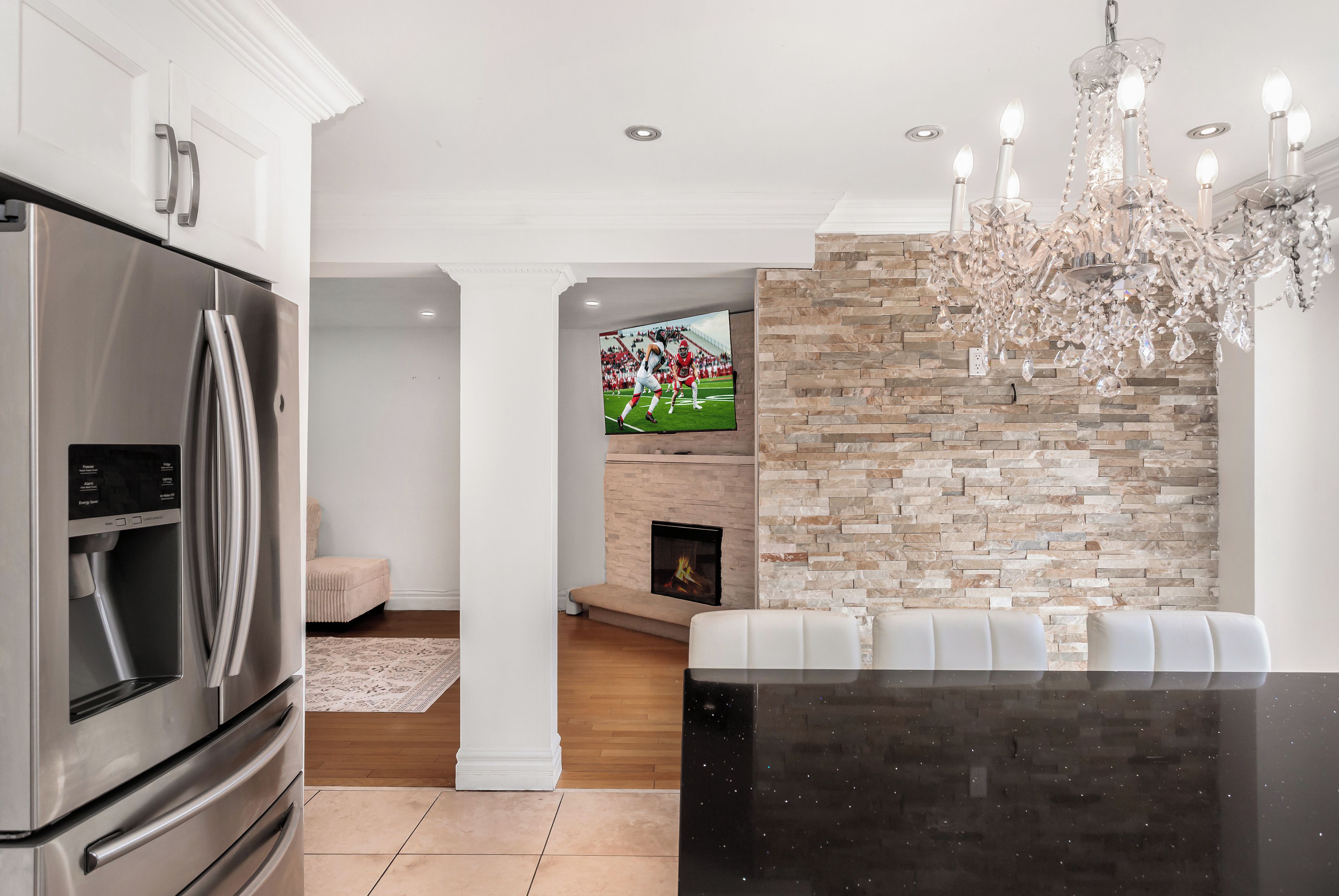 A modern kitchen with a stainless steel refrigerator, a stone accent wall, a fireplace, and a chandelier.