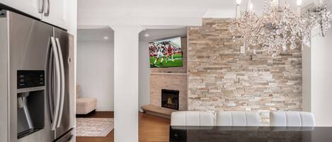 A modern kitchen with a stainless steel refrigerator, a stone accent wall, a fireplace, and a chandelier.