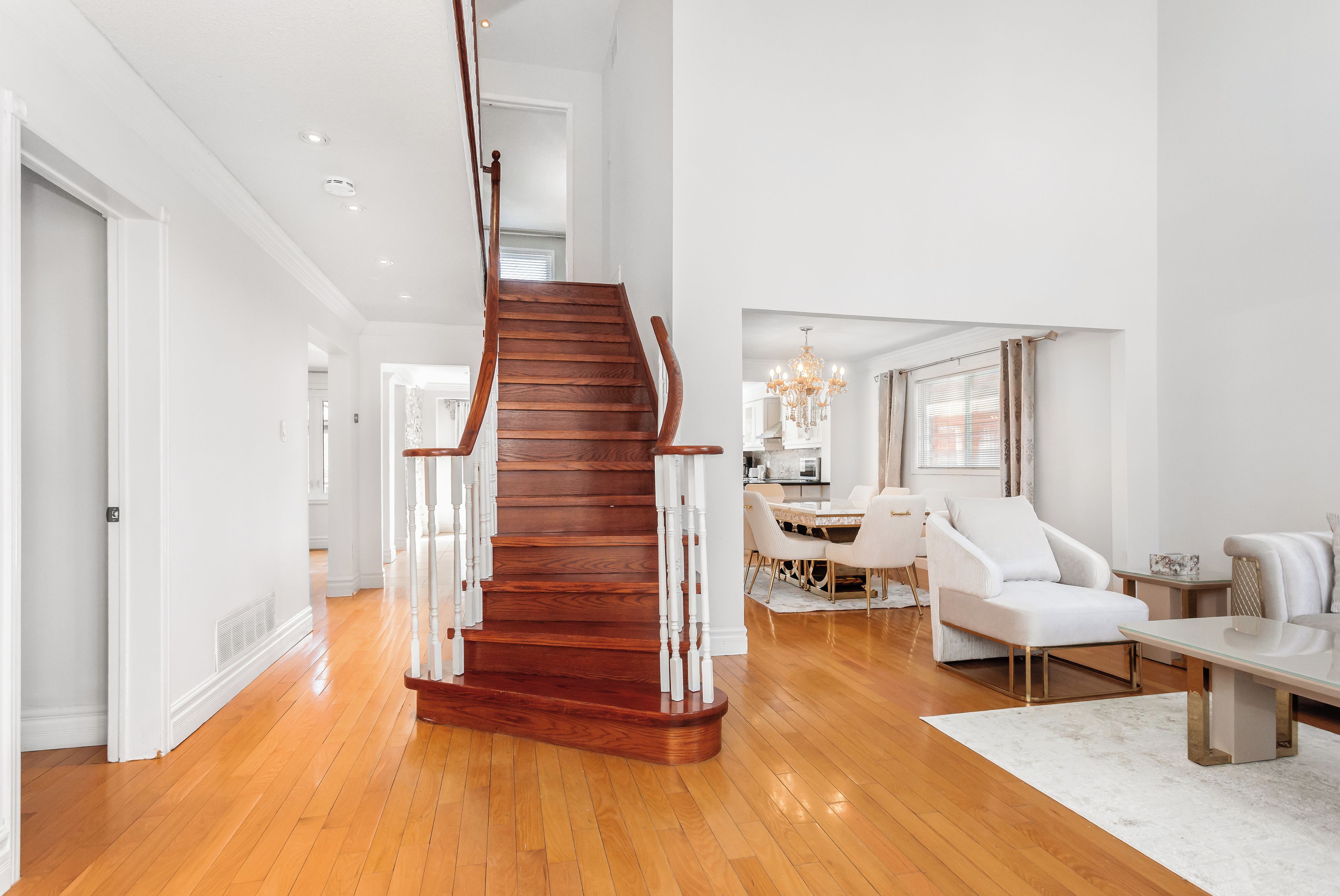 A spacious living area with a wooden staircase, a dining area, and a kitchen in the background.