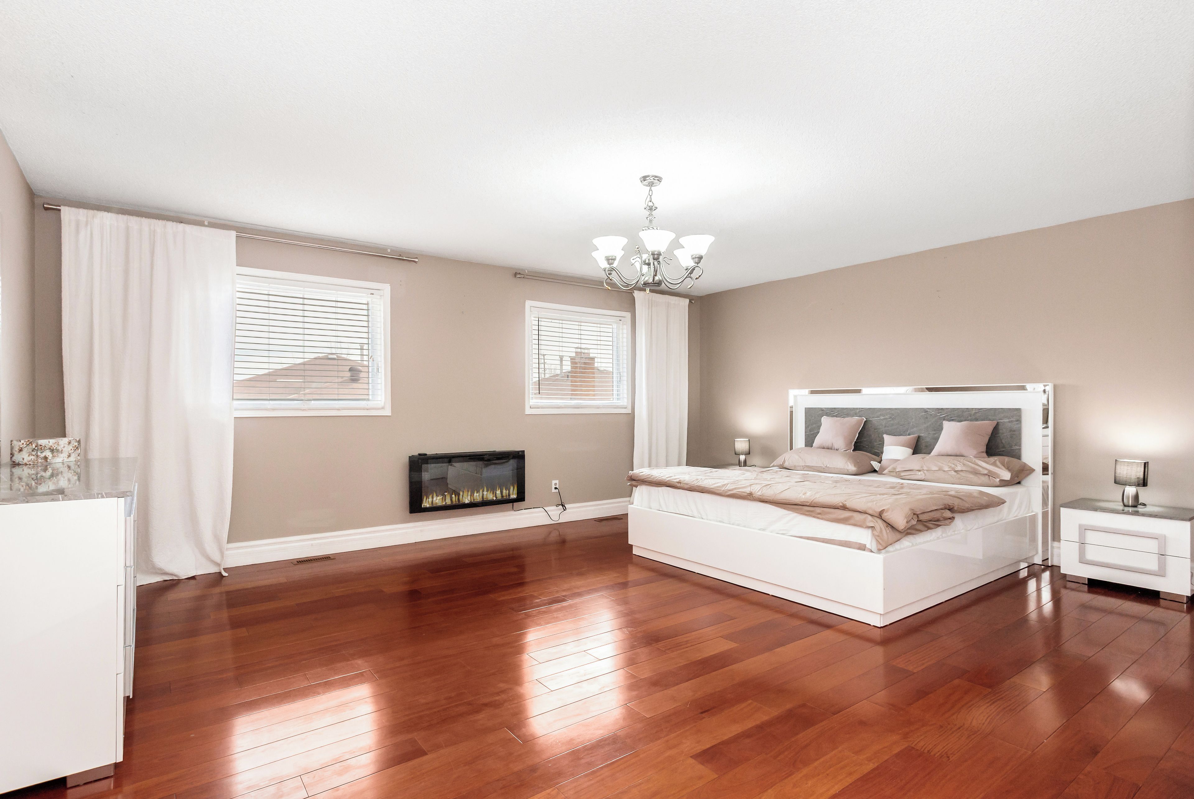 A bedroom with a large bed, a nightstand, a wall-mounted fireplace, and a chandelier.