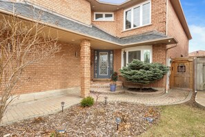 A two-story brick house with a front porch, a small tree, and a mailbox. - Executive 5BR Rose Bloom Haven with Private Deck (Mississauga)