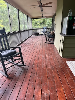 Eine Holzterrasse mit Deckenventilator, Grill und Sitzgelegenheiten im Freien.