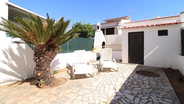 Un patio con suelo de piedra, sillas blancas y una palmera.