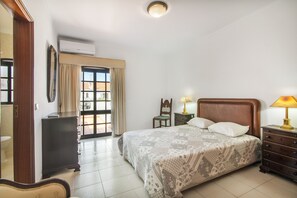 Une chambre à coucher avec un lit, des tables de chevet, une commode, un miroir et une fenêtre avec des rideaux.