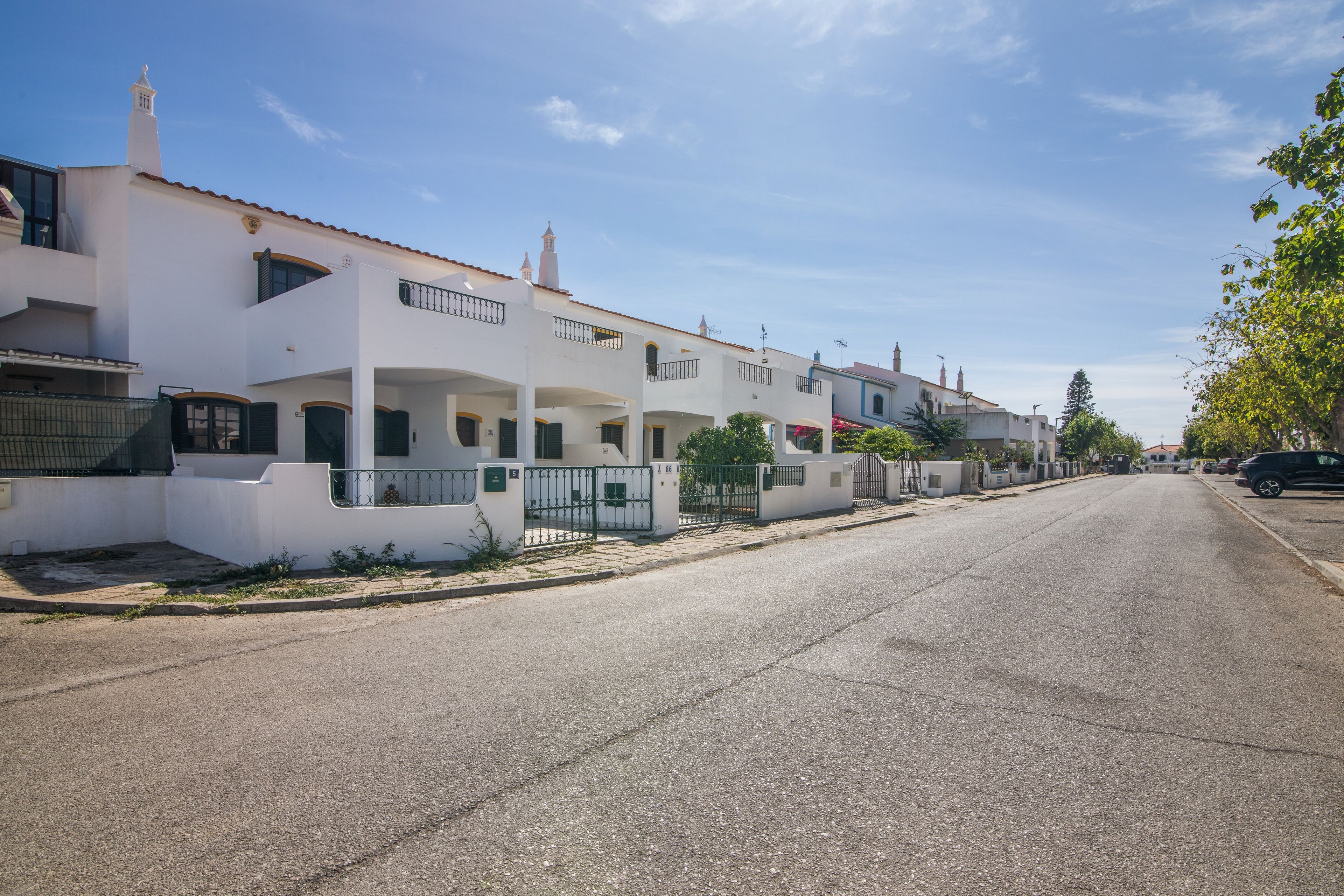 A residential street with white houses, a clear sky, and a parked car on the right.