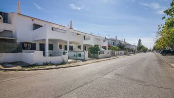 A residential street with white houses, a clear sky, and a parked car on the right.