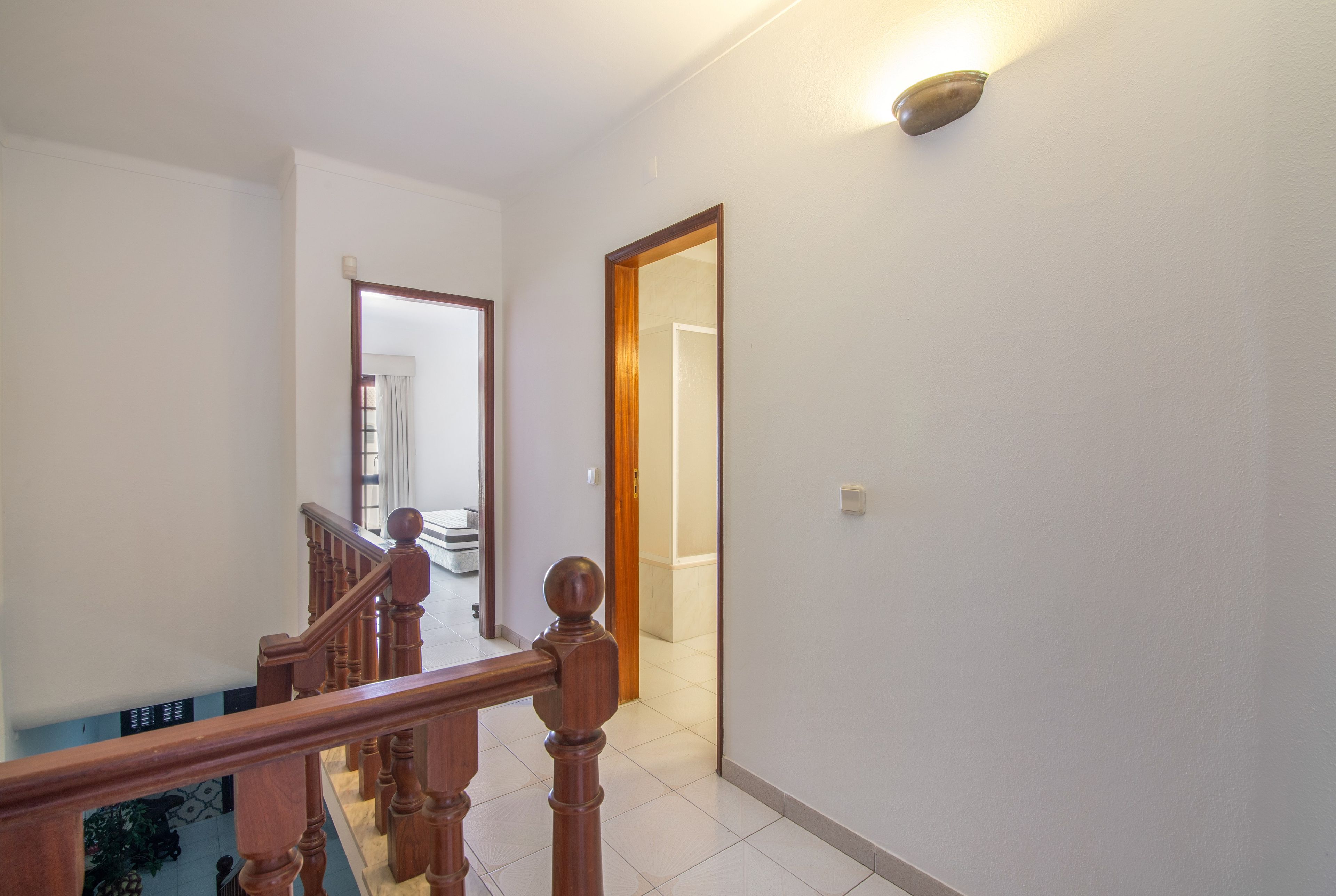 A hallway with a wooden staircase, a light fixture, and a door leading to another room.