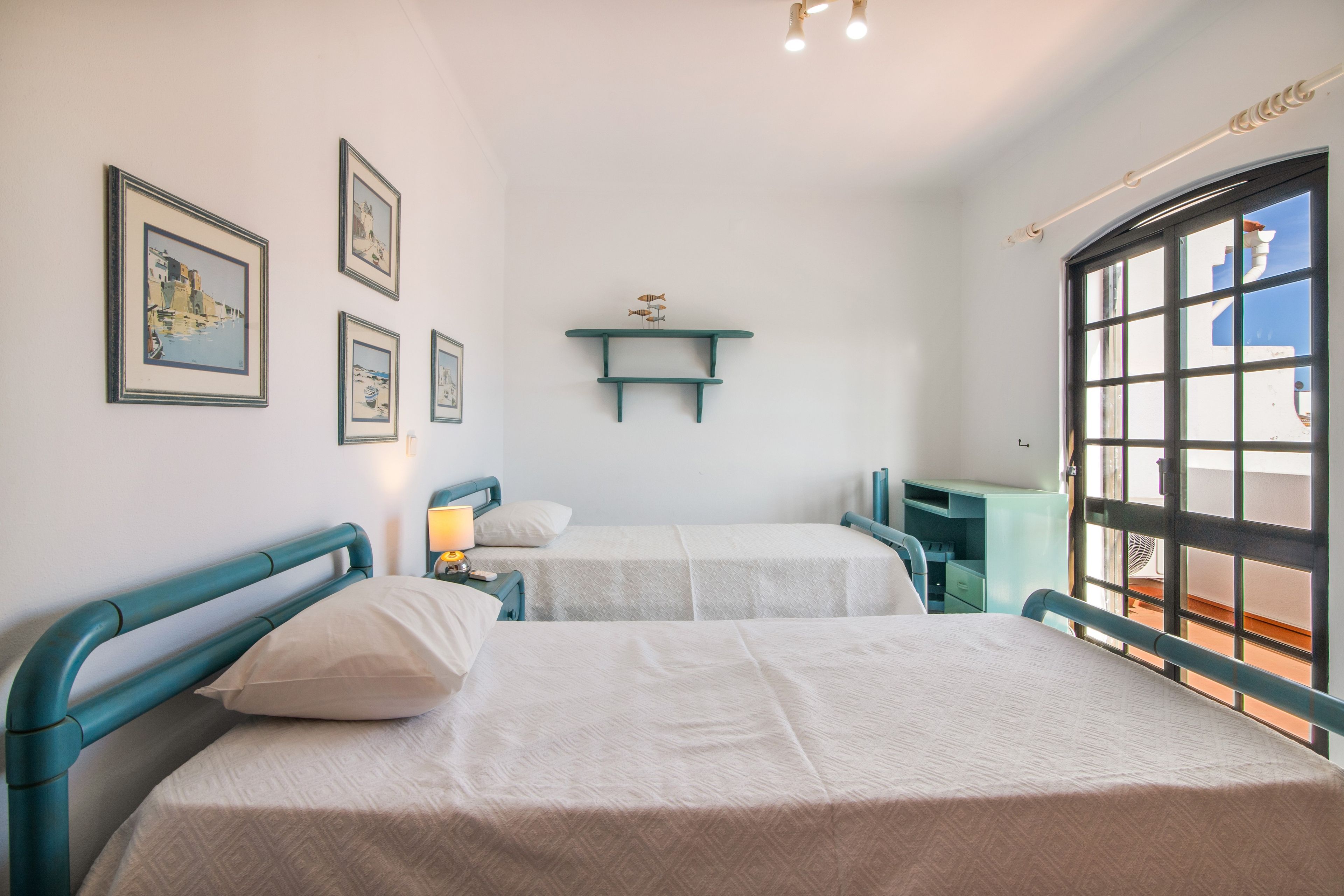 Una habitación con dos camas, una mesita de noche, una estantería con adornos y una ventana con vistas.