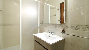 Un baño con lavamanos blanco, espejo y zona de ducha.