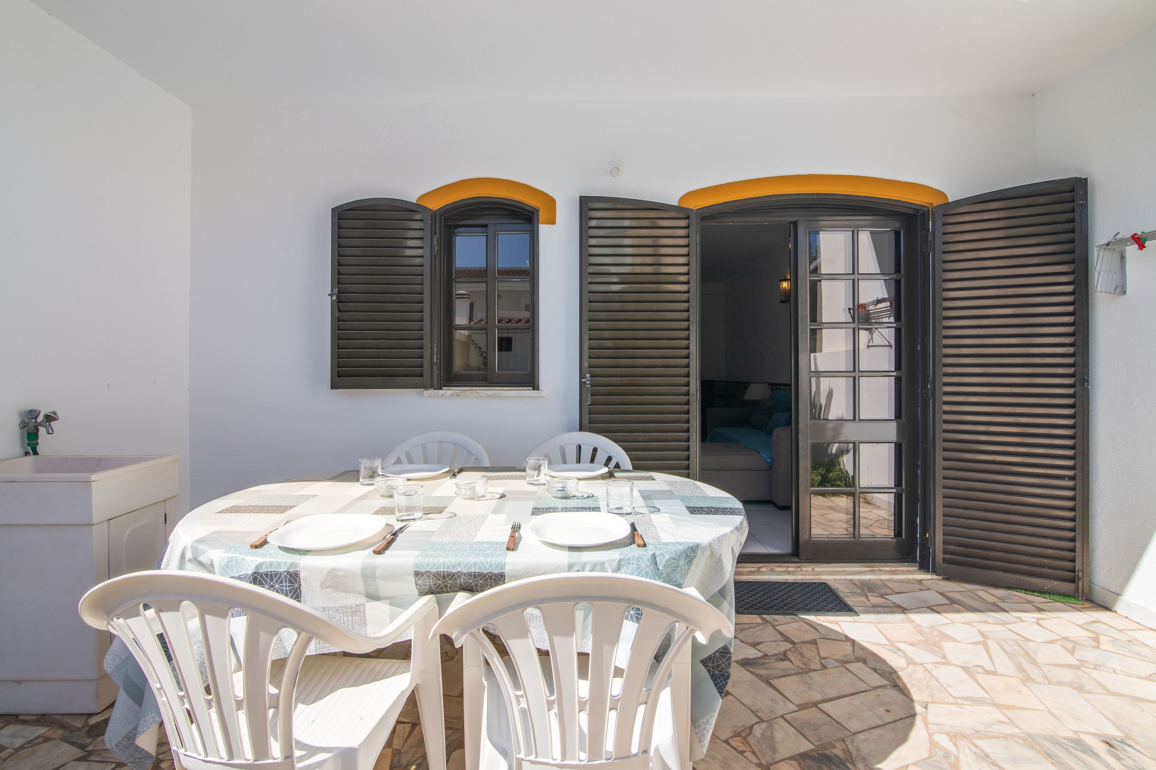 Un coin repas avec une table dressée pour quatre personnes, des chaises blanches et un sol carrelé.