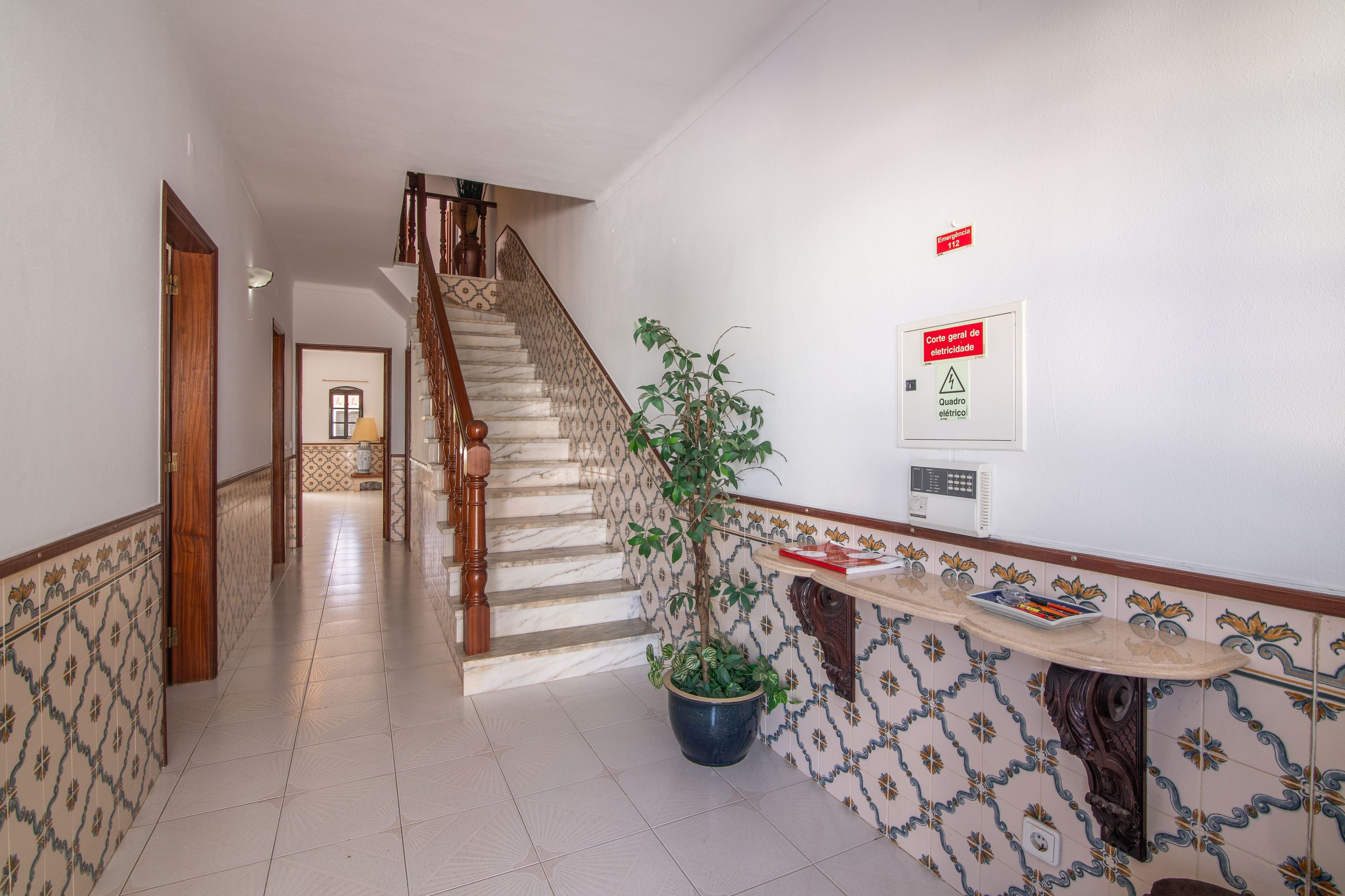 Un pasillo con una escalera de mármol, una planta en maceta y un letrero de emergencia en la pared.