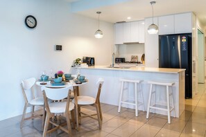 A modern kitchen with white cabinetry, a stainless steel refrigerator, and a dining area with a round table and bar stools.