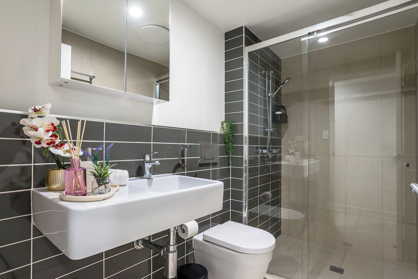 A modern bathroom with a white sink, a toilet, and a glass-enclosed shower.