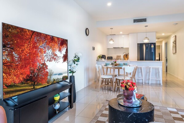 A modern living room with a large painting, a dining area with a white table and chairs, and a kitchen with white cabinets and a black refrigerator. - Fantastic 3-bedroom apartment with AC in charming West End (West End)