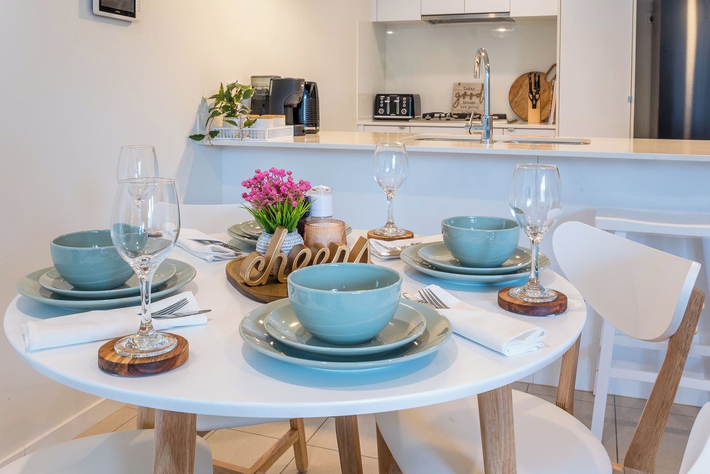 A dining table set with blue bowls, wine glasses, and wooden coasters.