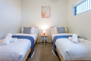 A hotel room with two single beds, a small bedside table with a lamp, and a window with blinds.