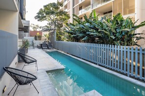 A swimming pool with a white fence, surrounded by greenery and a building with balconies. - Fantastic 3-bedroom apartment with AC in charming West End (West End)