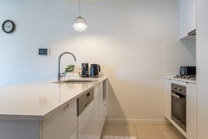 A modern kitchen with a white countertop, stainless steel appliances, a built-in oven, and a hanging pendant light.