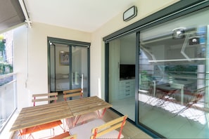 A balcony with a wooden table and chairs, a sliding glass door leading to a kitchen area, and a small framed picture on the wall. - Cozy 1-bedroom Apartment With A C Garage Near (Beausoleil)