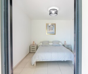 A bedroom with a bed, two bedside tables, a wall-mounted light fixture, and a framed picture on the wall. - Cozy 1-bedroom Apartment With A C Garage Near (Beausoleil)