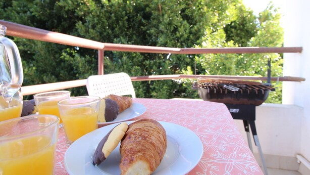 A table with a plate of food, a drink, and a grill. - Holiday Home 'Mantamar Beach Ap' with Balcony, Wi-Fi and Air Conditioning (Vila Nova de Cacela)